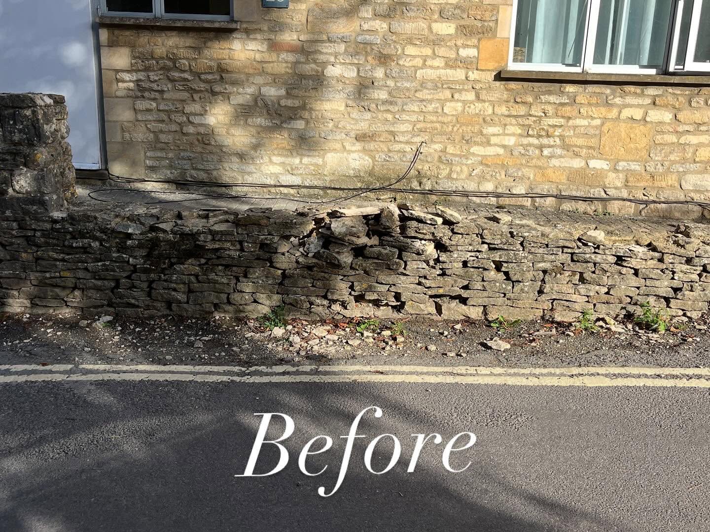 Roadside retaining drystone wall in Burford before repair, its top courses collapsed with loose stone spilling toward the kerb