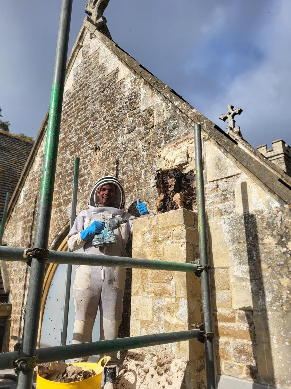 Mason in a bee suit on the scaffold beside the rebuilt section of pale ashlar stonework