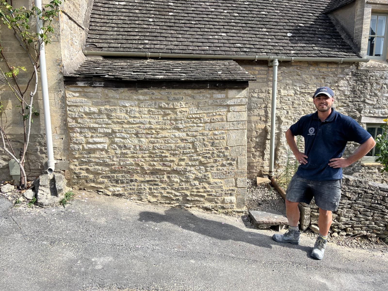 Elliot standing beside a Cotswold stone elevation he has repointed, the joints made good and the stone face clean