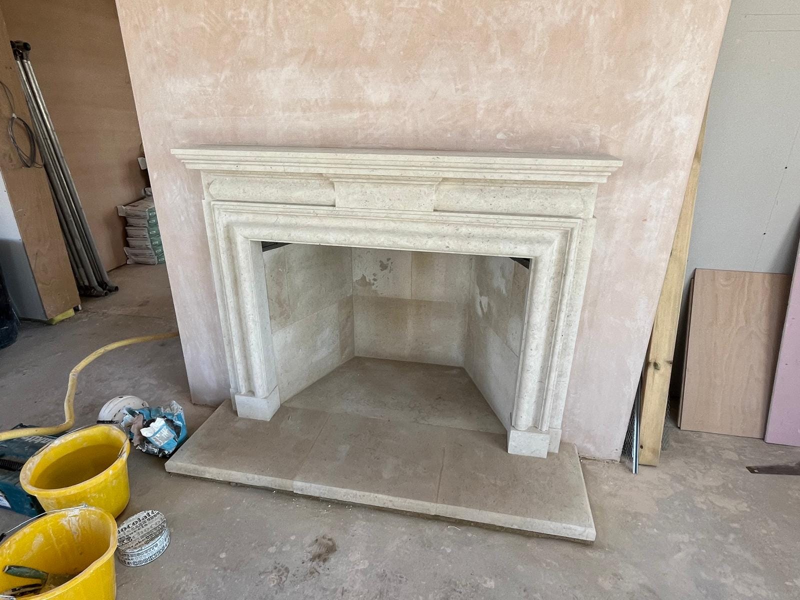 A bolection-moulded limestone fireplace surround with a plain frieze and mantel, installed against a pink-plastered chimney breast with a single-slab hearth