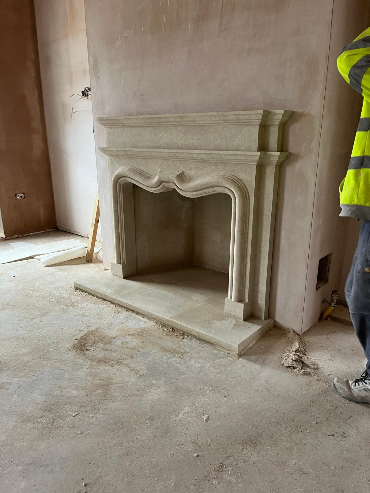 A limestone fireplace surround with an ogee arch opening and moulded mantel, against fresh plaster, with a large single-slab hearth