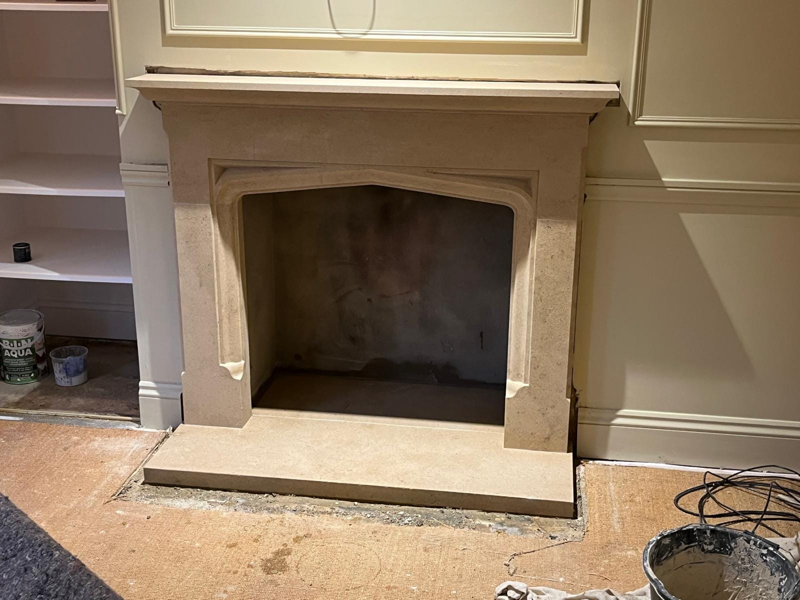 A stone fireplace surround with a four-centred arch, set into a panelled and painted room with a deep hearth slab