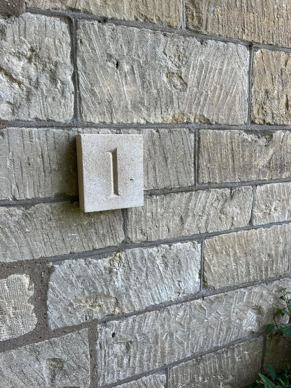 Square stone number plaque with a carved figure one, fixed to a coursed ashlar wall