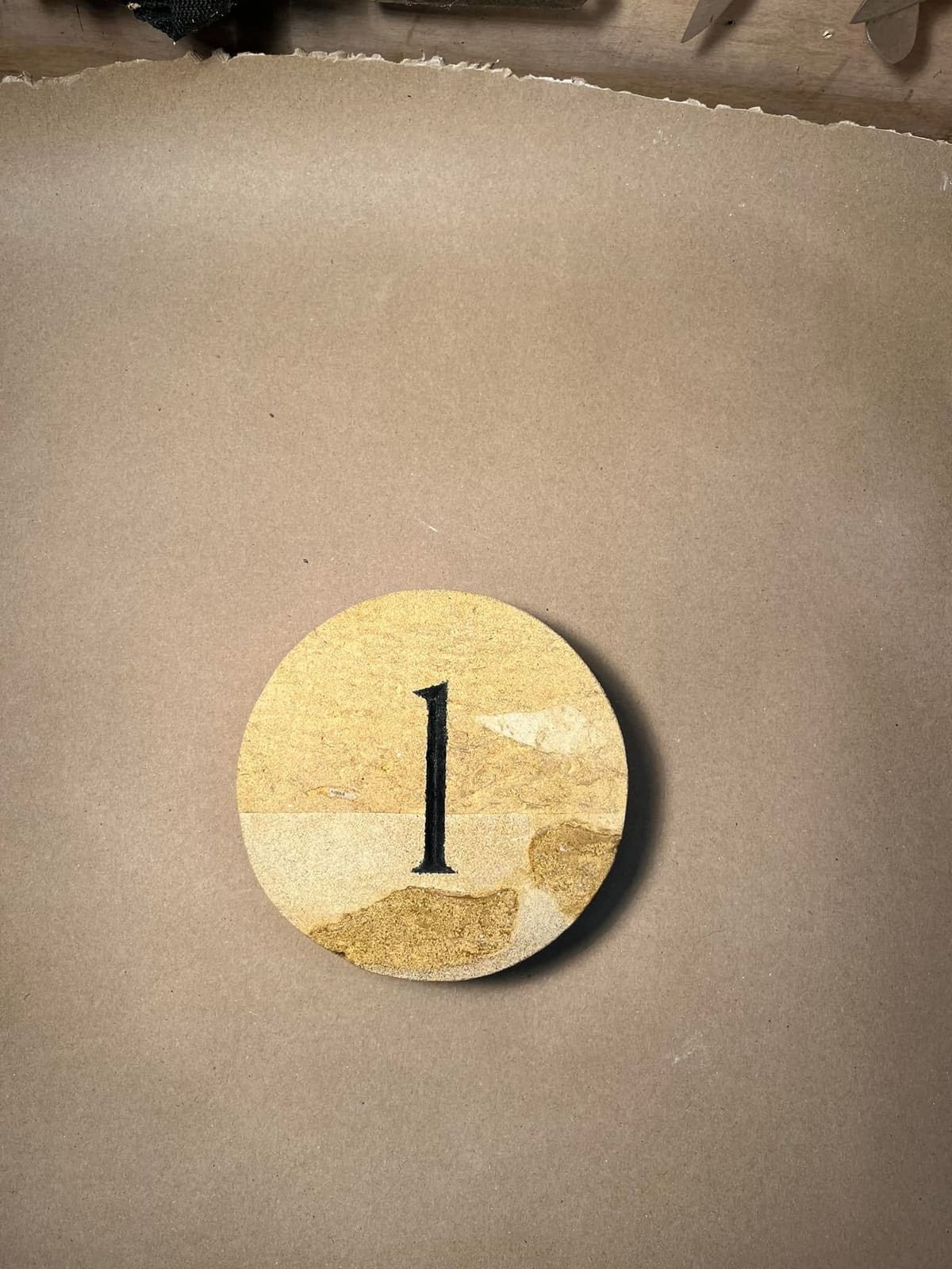 Round stone door number disc with a carved and painted figure one, on the bench in the workshop