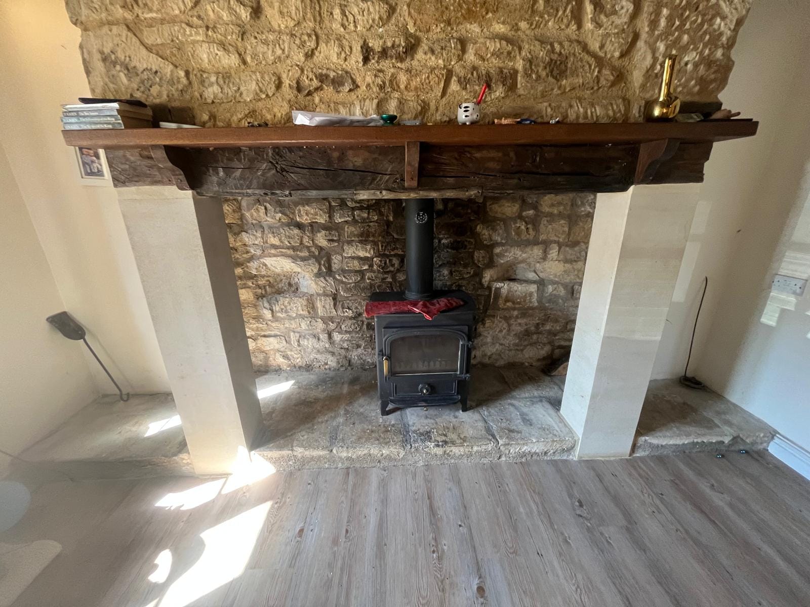 An opened-up inglenook with an oak bressummer beam, exposed stone rear wall, new stone jambs either side and a wood burning stove on a flagstone hearth