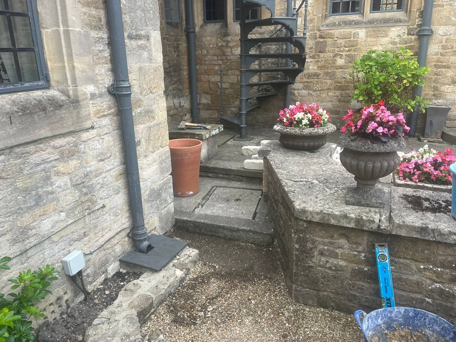 Courtyard at the Lamb Inn, Burford, before the work: bare ground beside the downpipe where new walling is to go, existing planter wall to the right