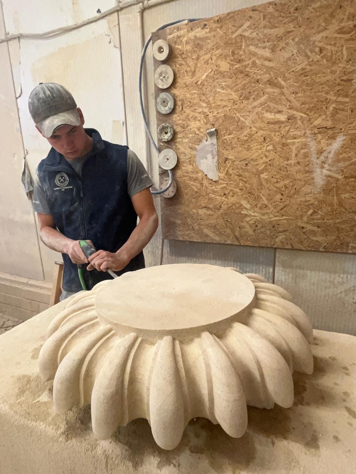 Charlie refining the same carved stone base with an air chisel, working between the lobes