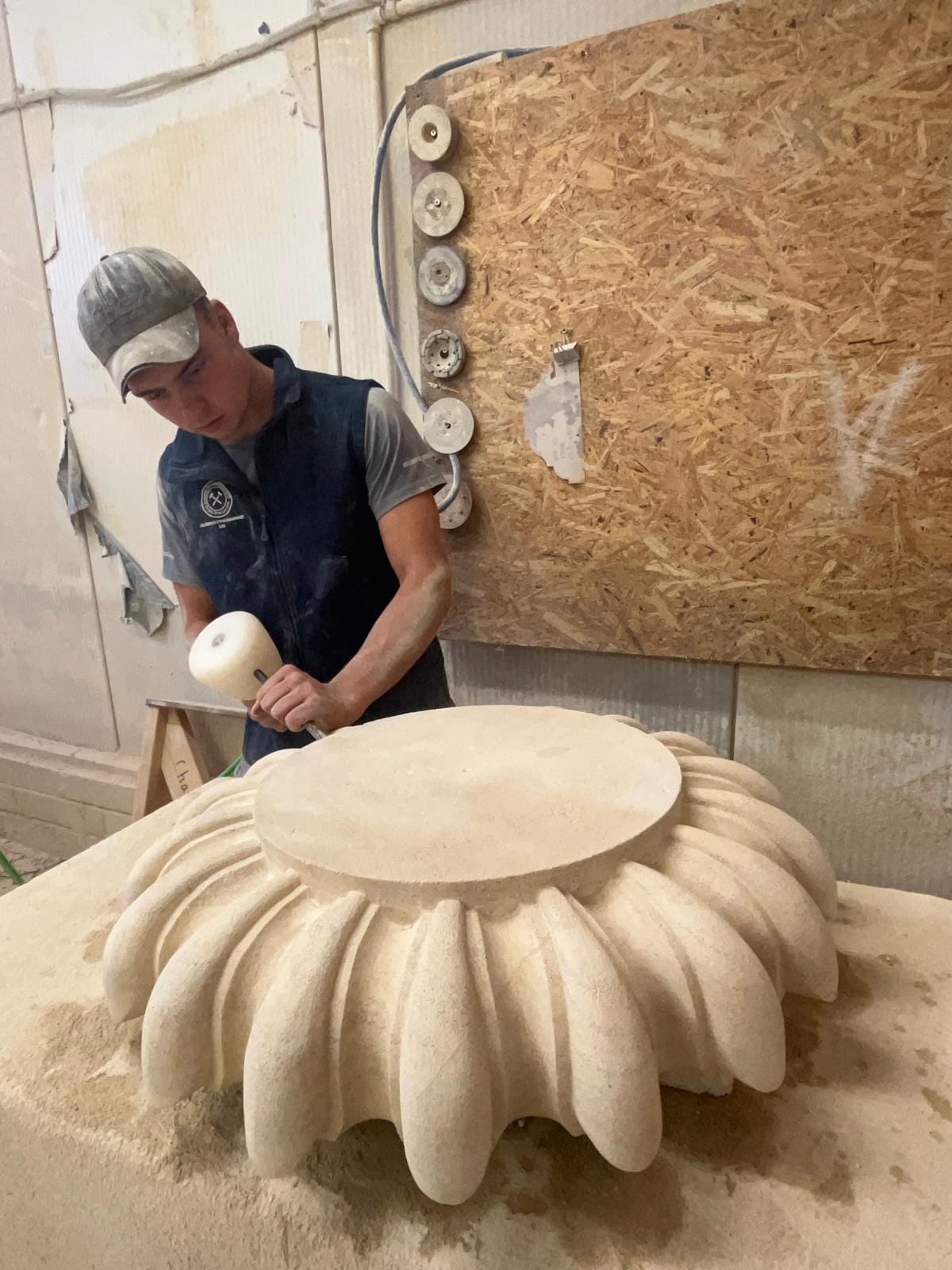 Mason working a large carved stone piece with a mallet and chisel at the bench