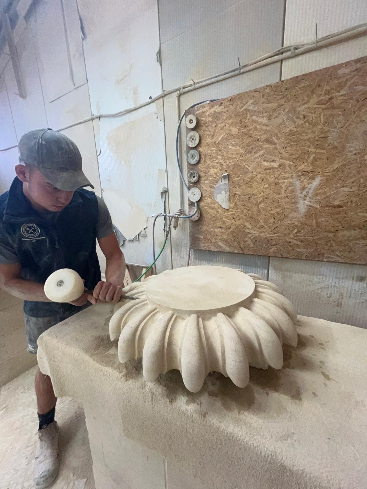 Charlie working a carved stone base with a mallet and chisel at the workshop bench, the piece cut with deep rounded lobes