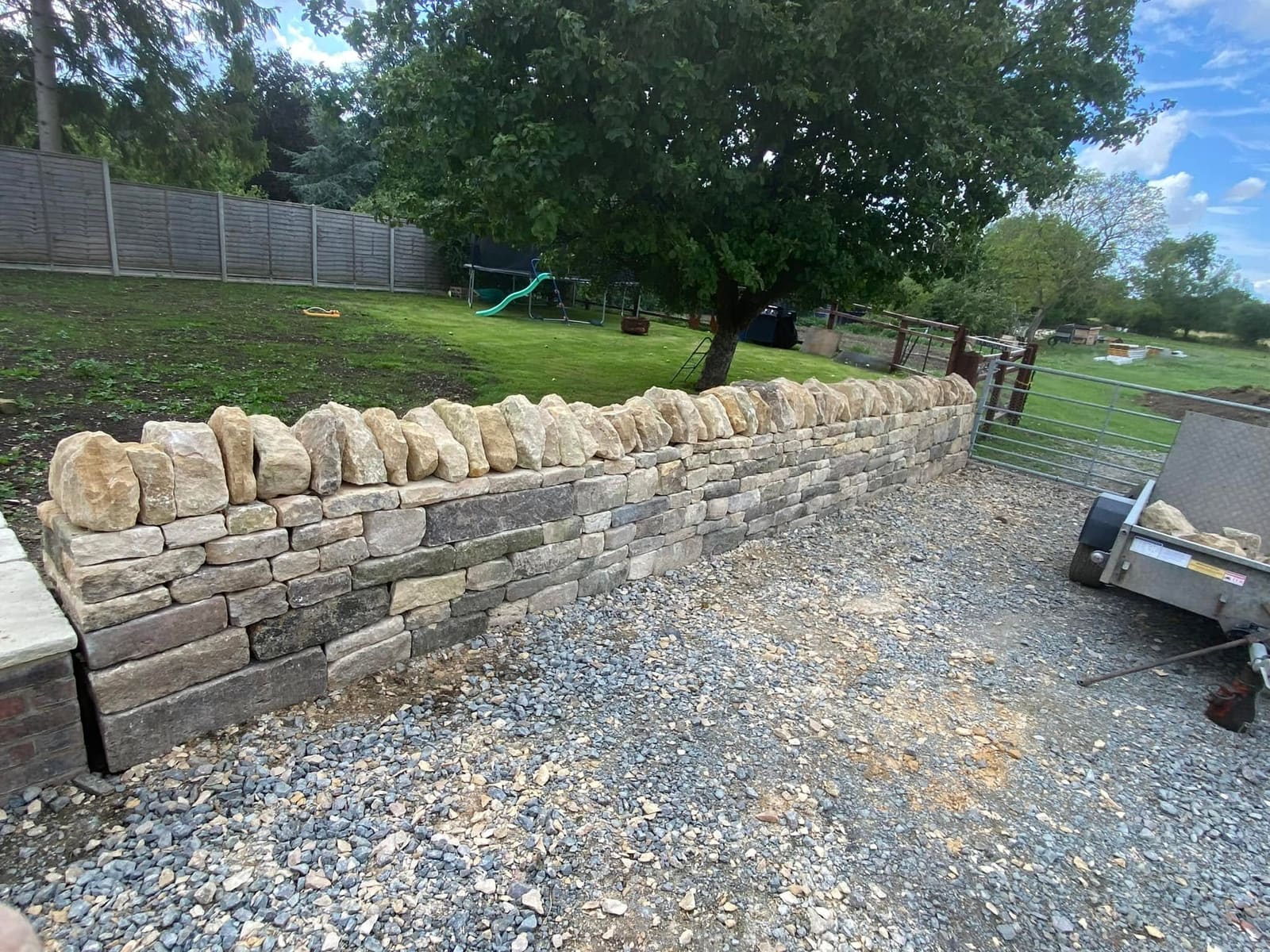 The finished dry stone wall seen along its length from the drive, upright coping stones running the full run