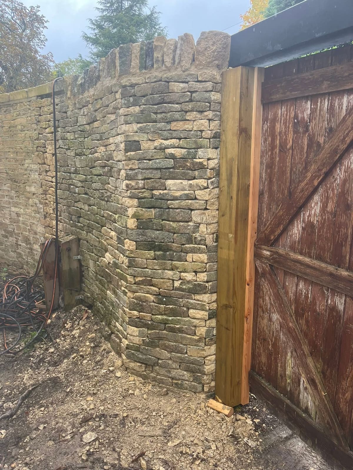Newly built dry stone wall cheek beside a new timber gate post, with coping stones set along the top
