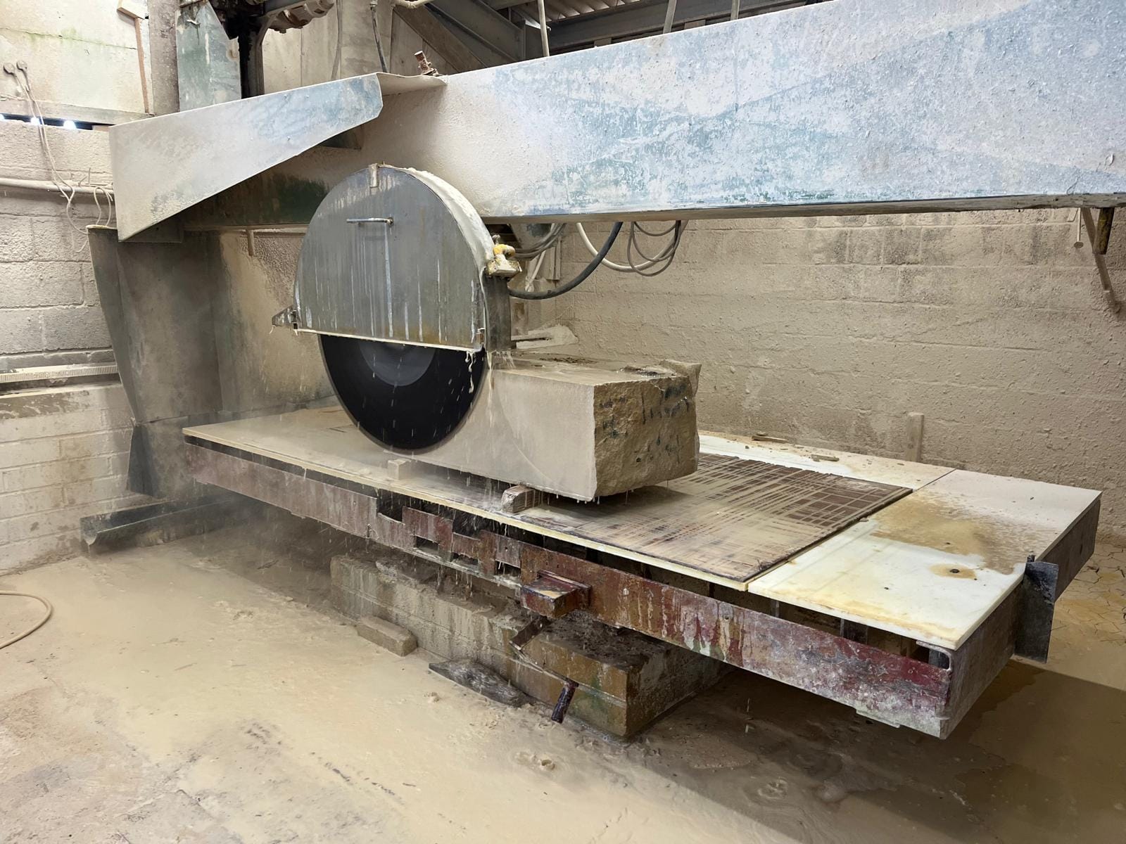 Water-cooled bridge saw cutting a block of limestone in the workshop